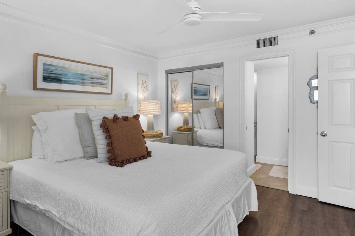 A bedroom with a large bed, white bedding, a ceiling fan, and a door with a mirror.