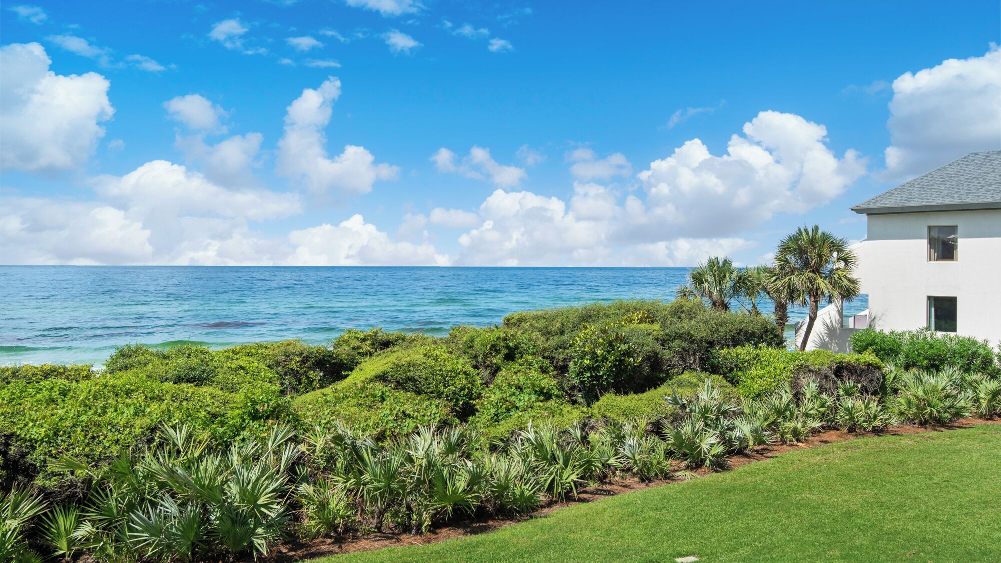 A coastal property with a white building, lush greenery, and a view of the ocean.