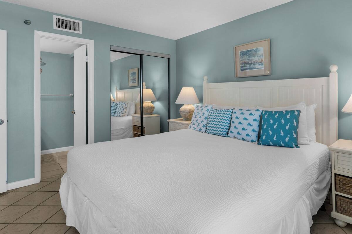 A bedroom with a large bed, two bedside tables with lamps, a wardrobe, and a mirror.