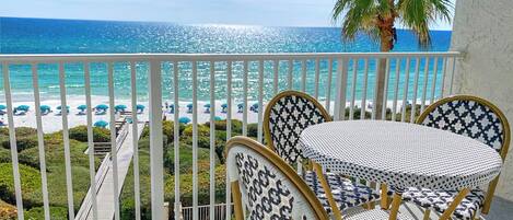 Un balcon avec vue sur la plage et l’océan. On y trouve deux fauteuils en osier et une petite table.