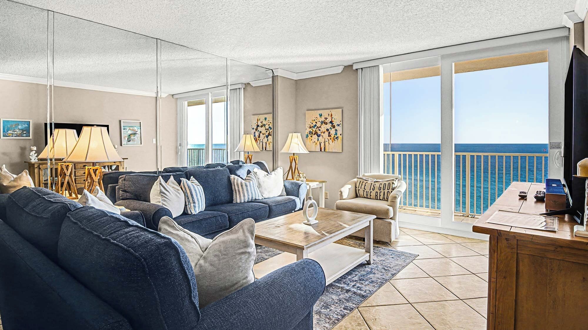 A spacious living room with a large sofa, a coffee table, and a view of the ocean through large windows.