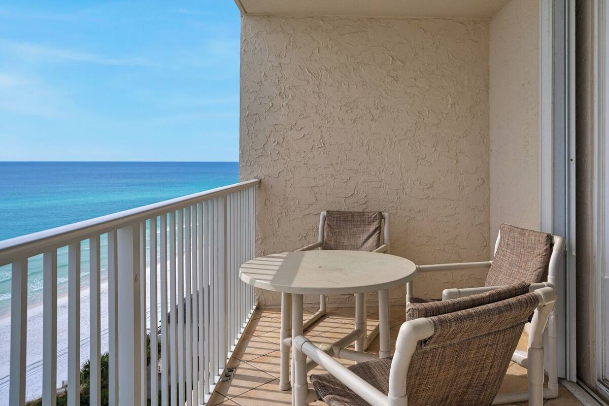 A balcony with a white railing, a round table, and two wicker chairs.
