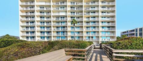 A multi-story hotel with balconies, a wooden boardwalk, and lush greenery.