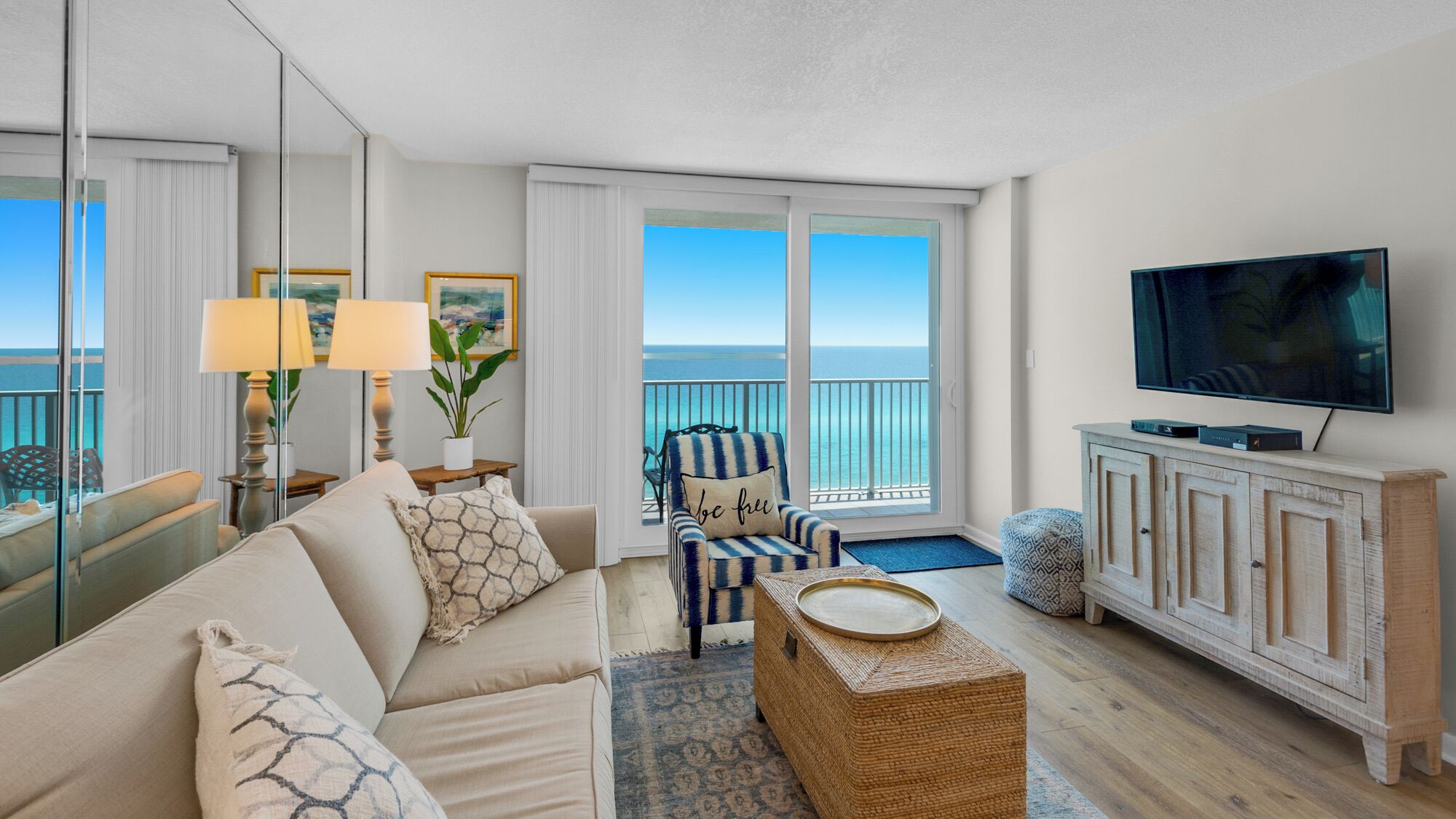 A modern living room with a large sofa, a striped armchair, a television, and a view of the ocean through large windows.