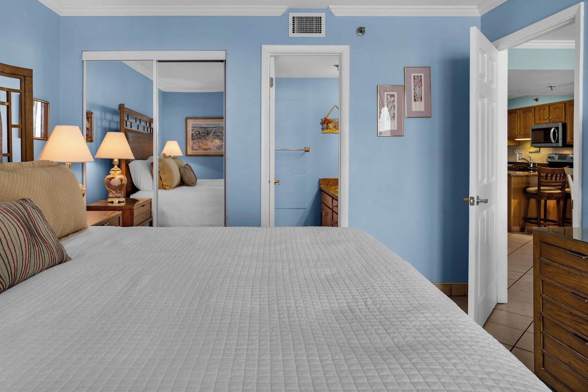 Un dormitorio con una cama grande, lámparas de noche, cabecera de madera, mesita de noche y cómoda.