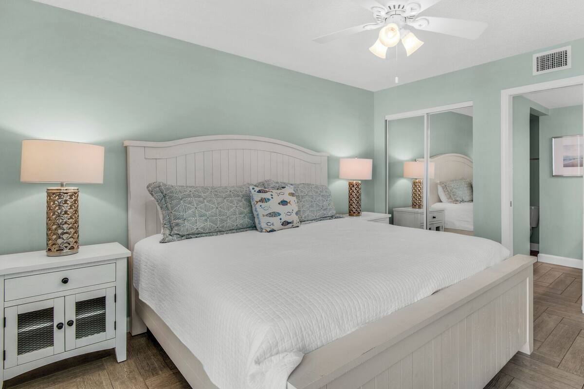 A bedroom with a bed, two bedside tables, a ceiling fan, and a door.