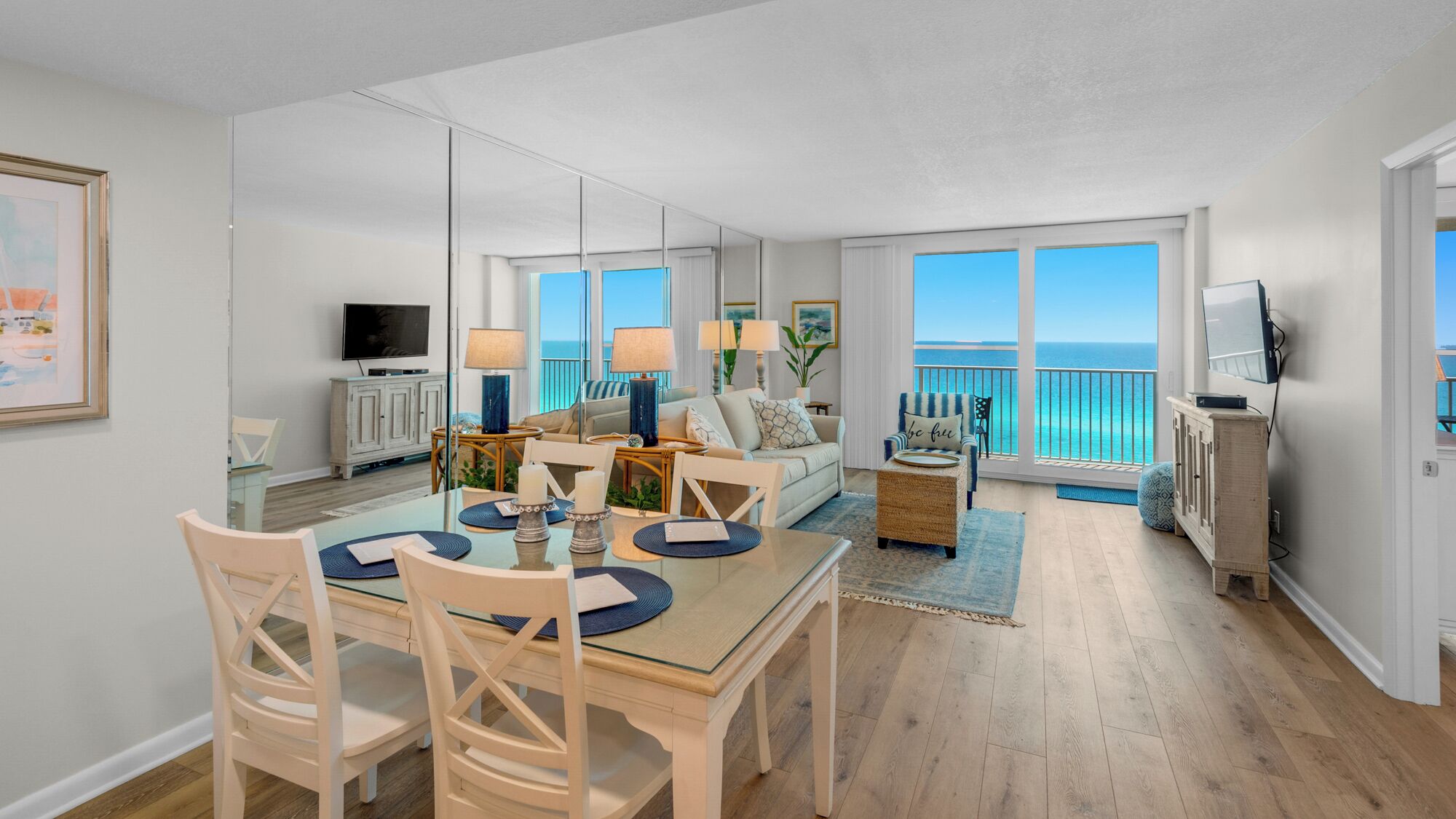 A spacious living area with a dining table, chairs, a sofa, and a TV. There are large windows with a view of the ocean.
