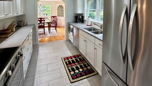 A modern kitchen with stainless steel appliances, white cabinetry, and a wooden dining area visible through an archway. - Hard Aground - Ocean View Cottage in Southwest Harbor! Pet Friendly!!!  (Southwest Harbor)