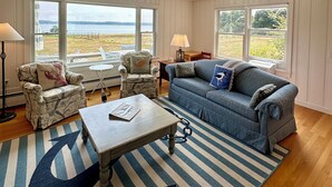 A living room with a view of the sea, a sofa, armchairs, a coffee table, and a striped rug. - Hard Aground - Ocean View Cottage in Southwest Harbor! Pet Friendly!!!  (Southwest Harbor)
