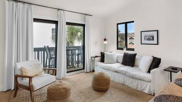 Een moderne woonkamer met een bank, een fauteuil, een bijzettafeltje en een balkon met tuinmeubilair.