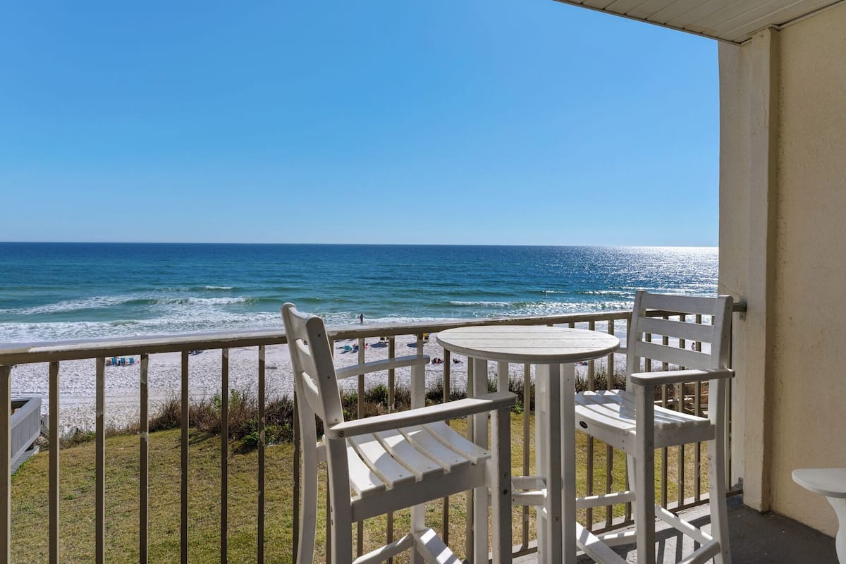 A balcony with a view of the ocean, featuring a round table and two chairs.