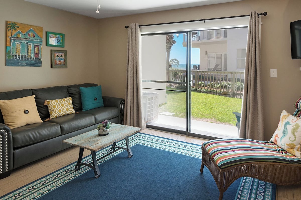 A living room with a sofa, a wicker chair, a coffee table, and a TV.