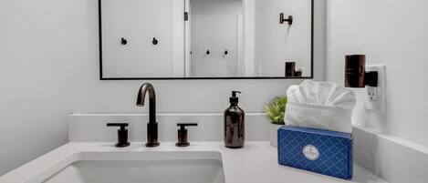 A modern bathroom with a white sink, black faucets, a mirror, and a blue box with a logo.
