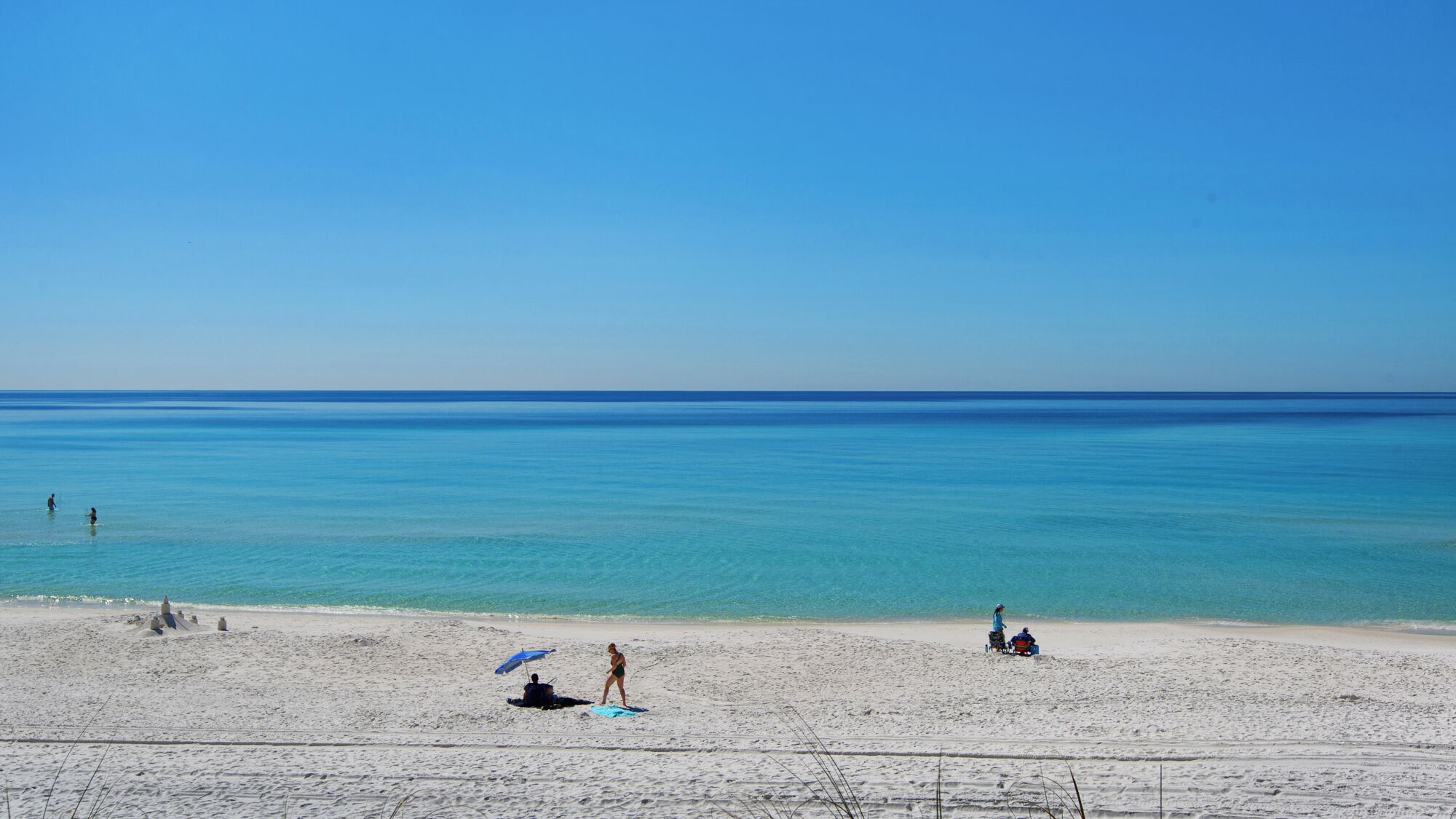 A beach with clear blue water, sandy shore, and a few people.