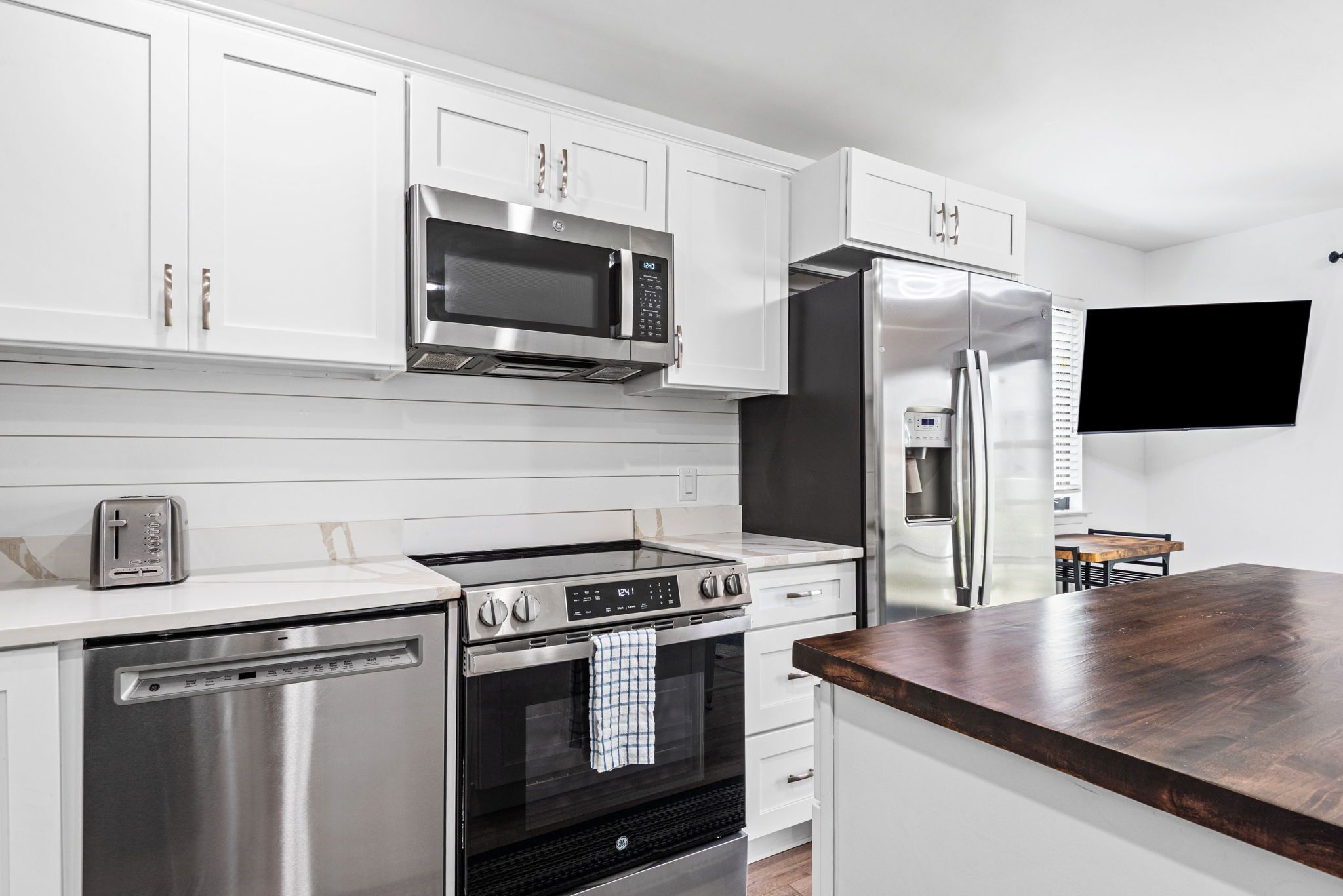 A modern kitchen with stainless steel appliances, white cabinetry, and a wooden countertop.
