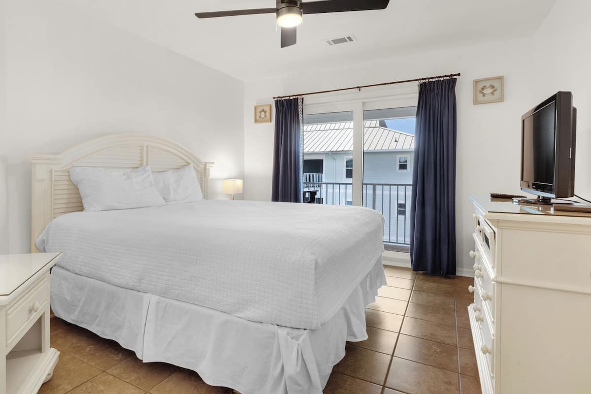 A hotel room with a bed, bedside tables, a TV, and a balcony with curtains.