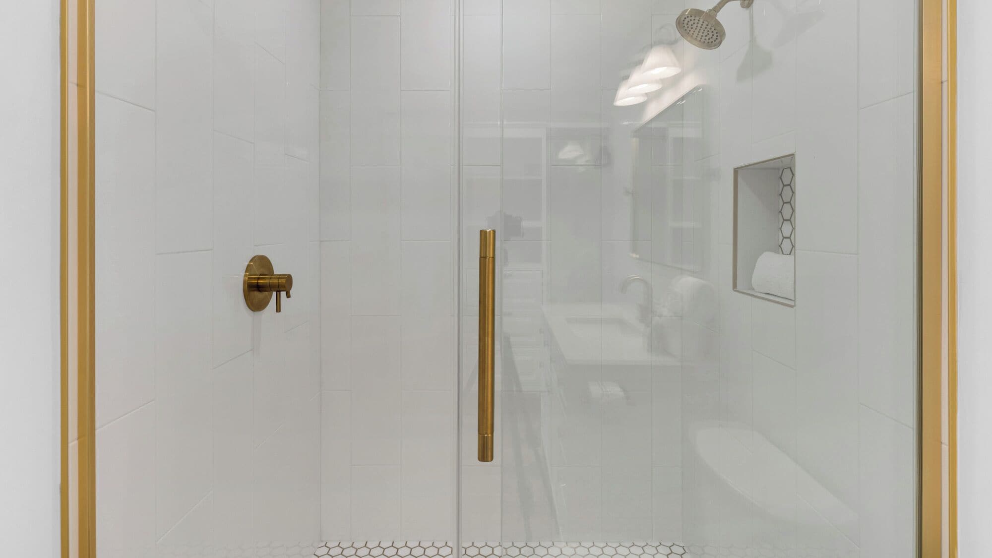 Une salle de bain moderne avec une douche à parois de verre, une poignée de porte dorée et un porte-serviettes mural.
