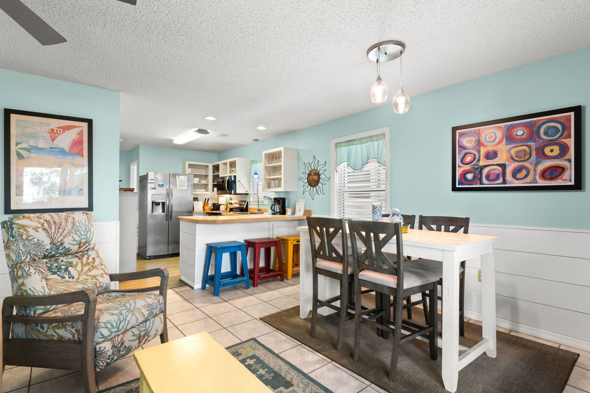 A kitchen with a refrigerator, a dining table with chairs, and a kitchen island with stools.