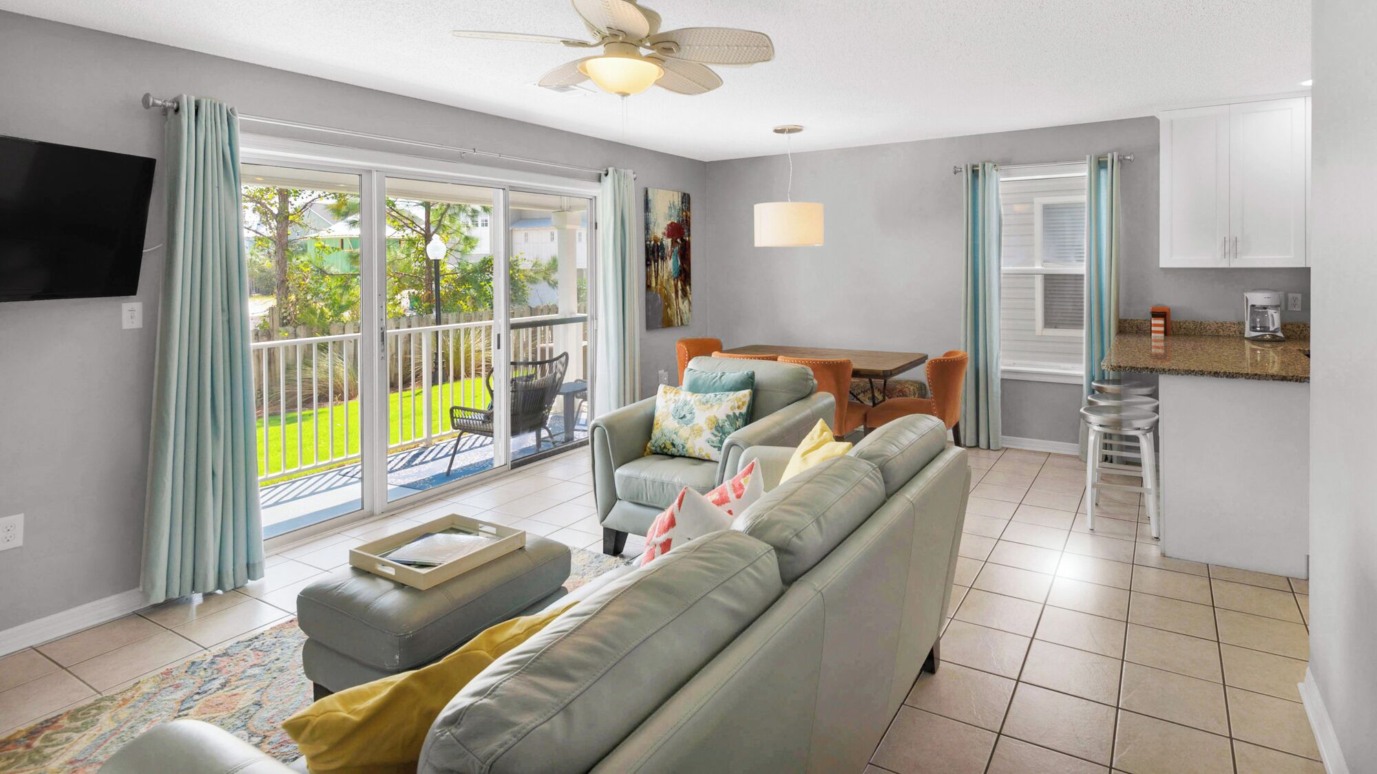 A modern living room with a grey sofa, a coffee table, and a dining area with a table and chairs. There is a kitchen area with a countertop and a coffee machine.