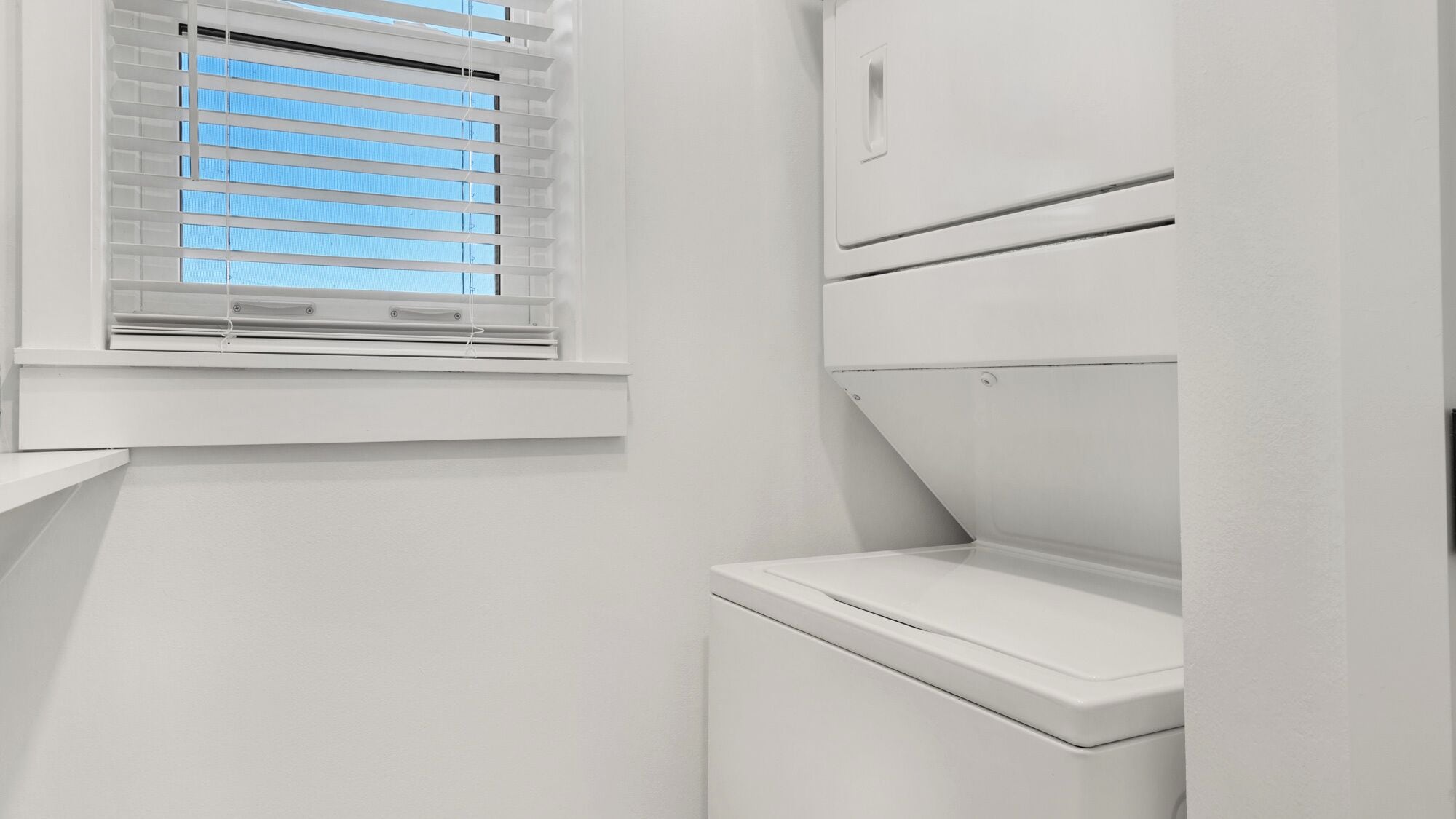 A white bathroom with a window, a toilet, and a shower area.