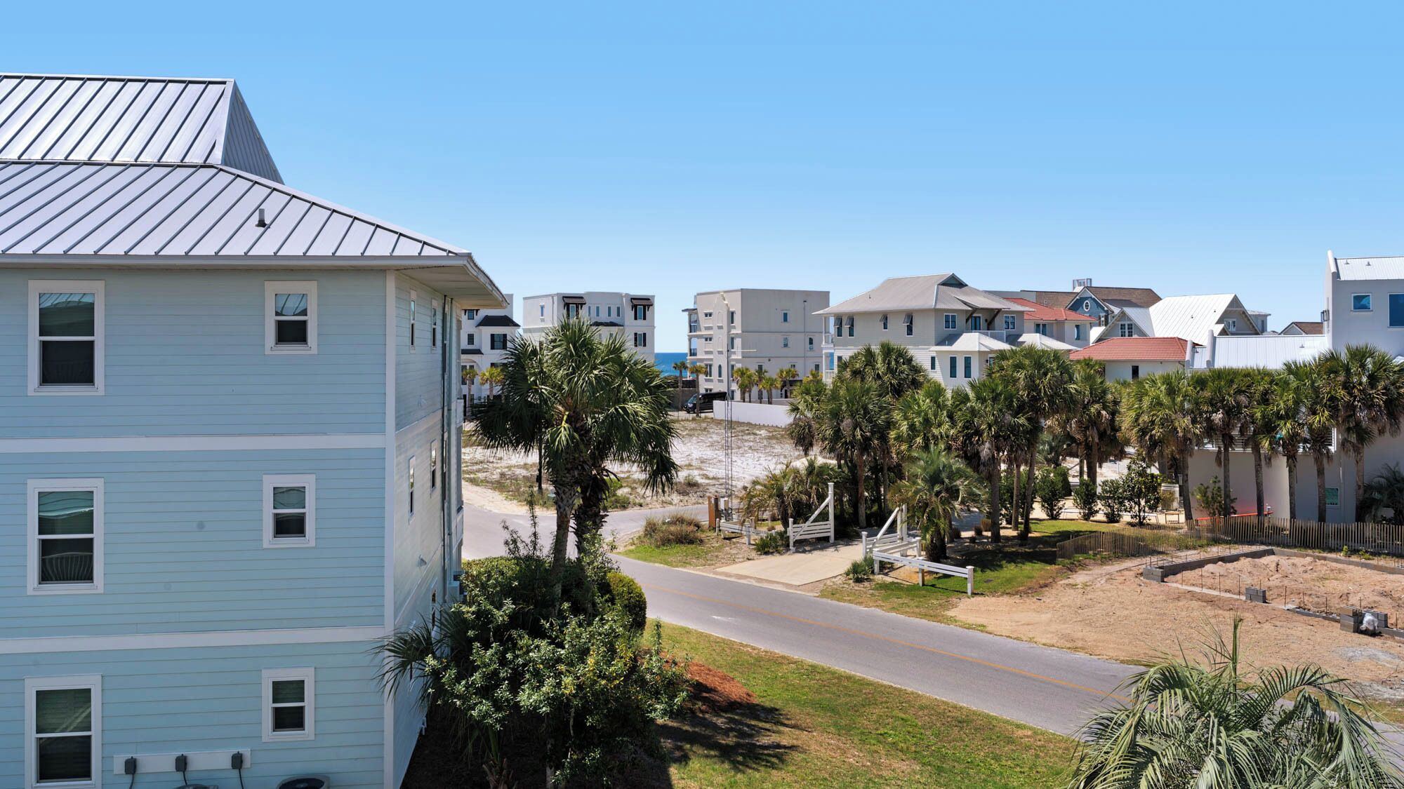 A coastal residential area with multi-story buildings, a road, and palm trees.