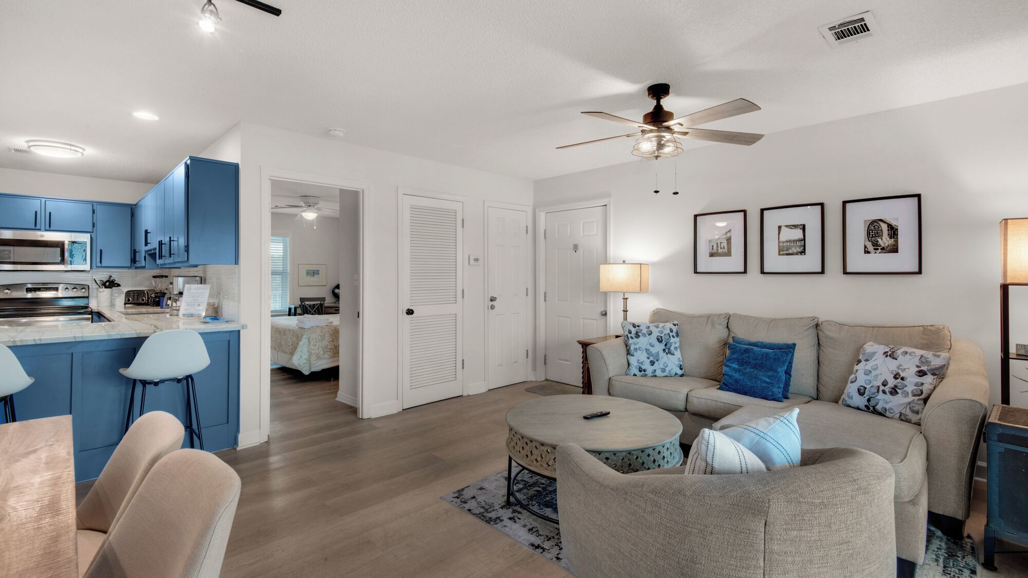 A modern living room with a sofa, coffee table, and a kitchen area with blue cabinets and a microwave.