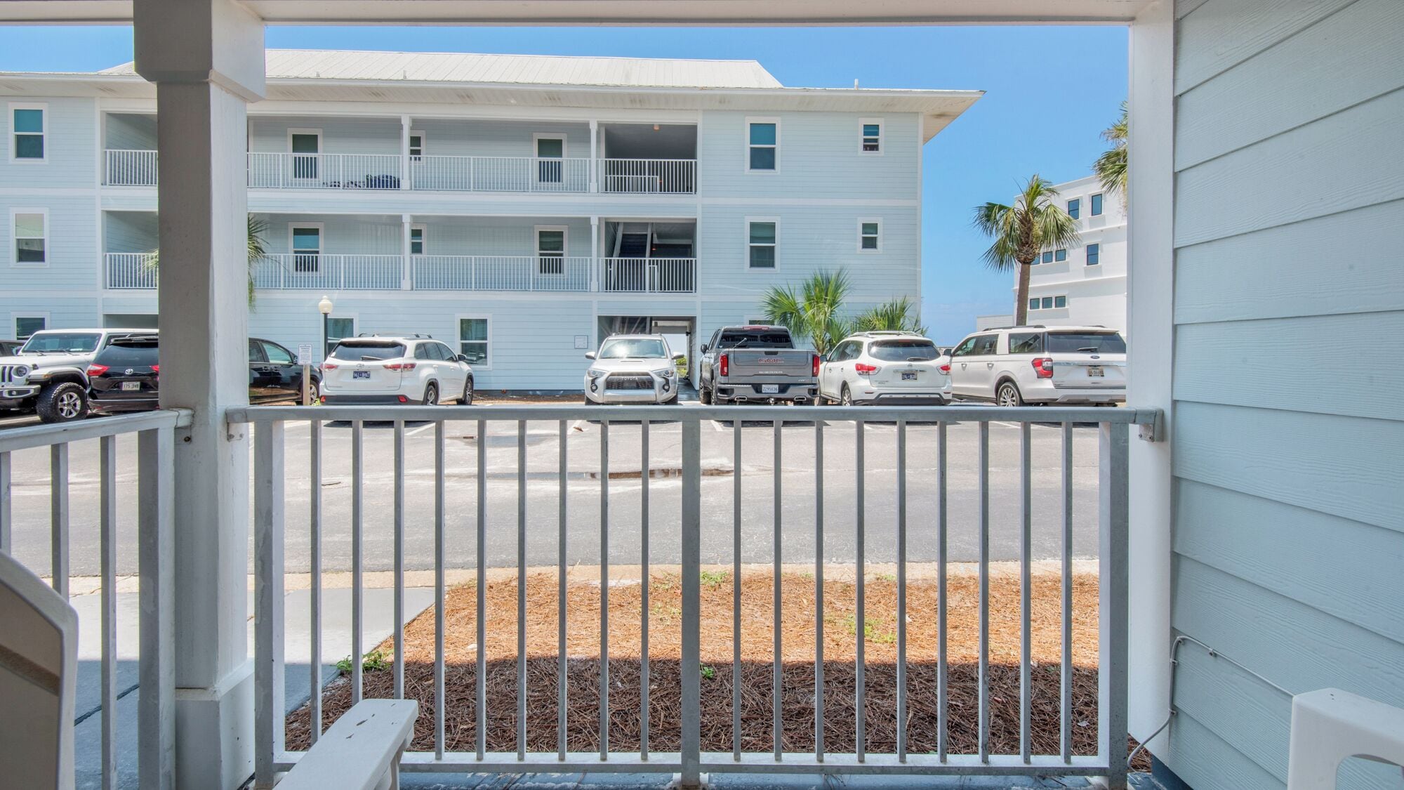 A view of a parking lot with several cars parked in front of a multi-story building with balconies.