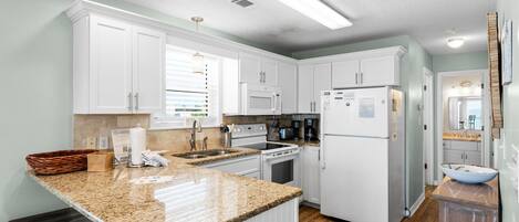 A modern kitchen with white cabinets, granite countertops, a built-in oven, microwave, and refrigerator.
