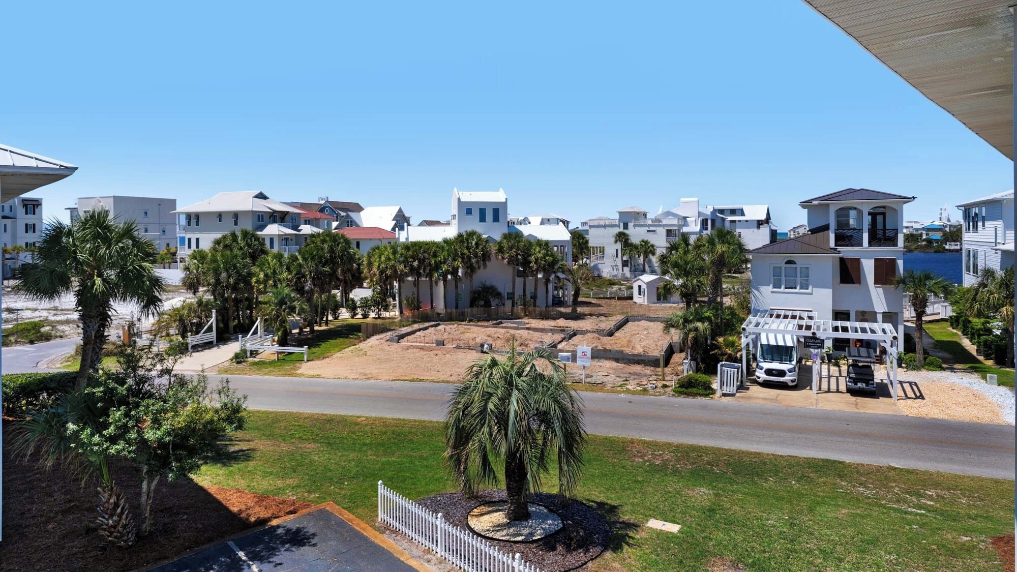 A residential area with modern houses, a sandy area possibly for construction, and a small tree in the foreground.