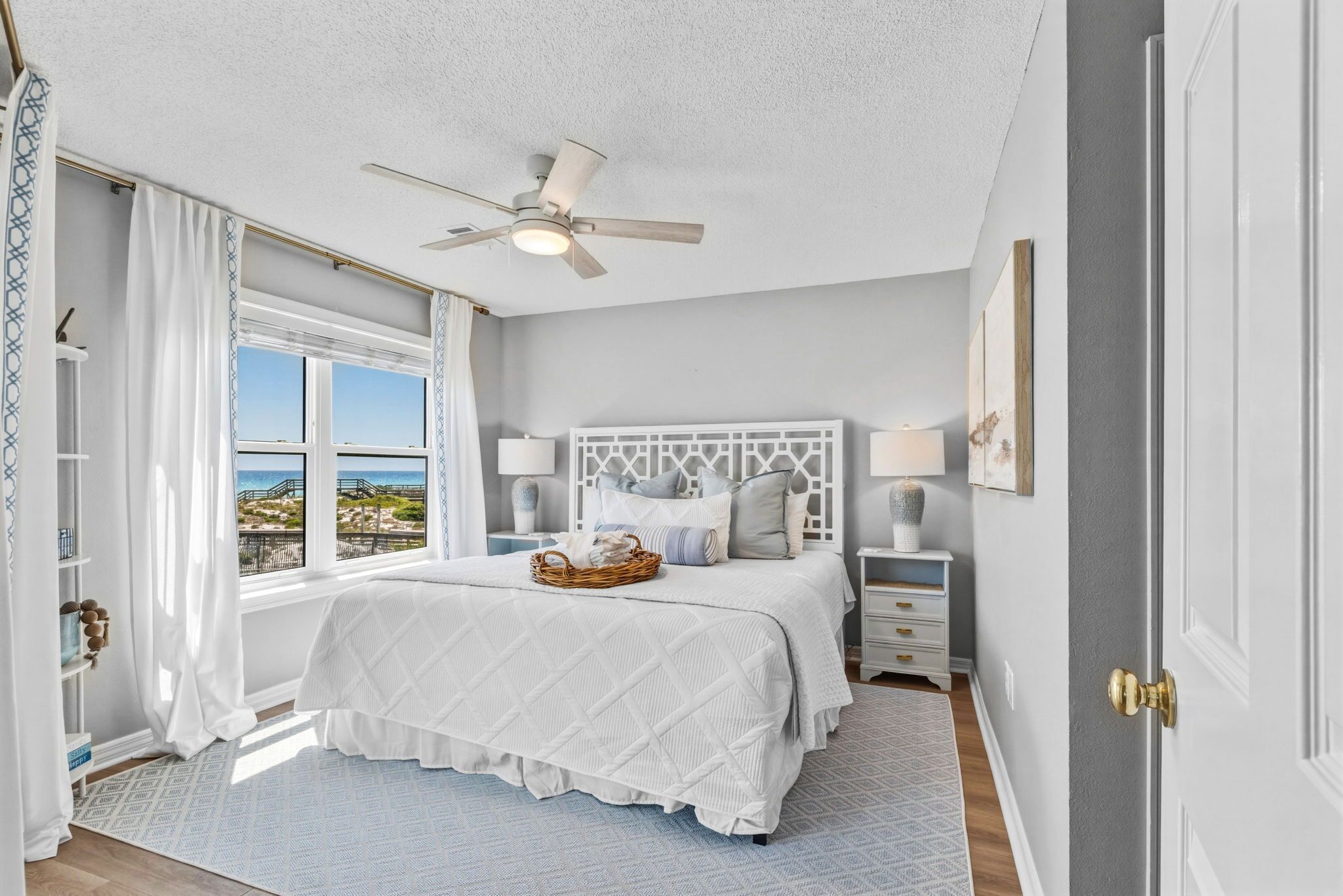 A bedroom with a bed, a ceiling fan, a window with a view, a nightstand, and a door.