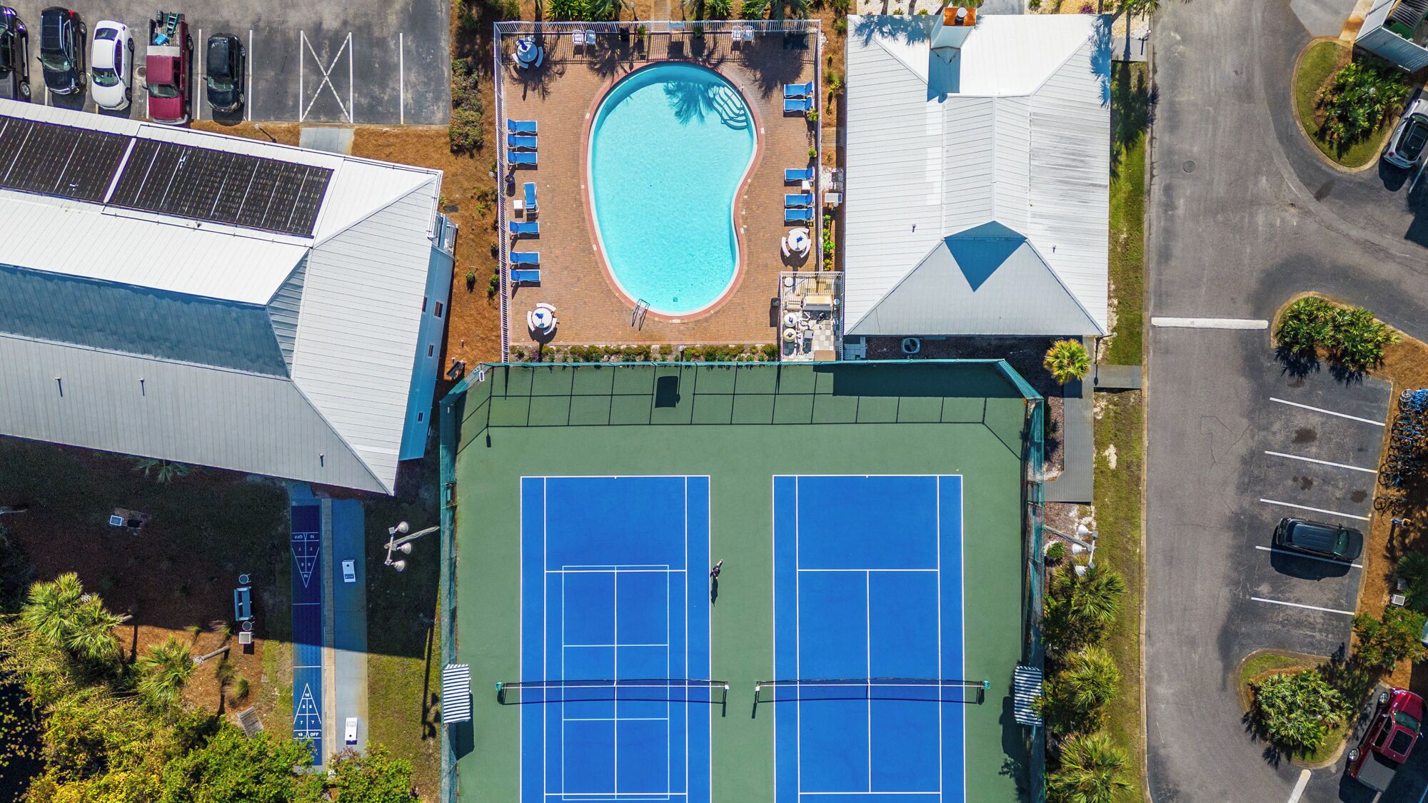 An aerial view of a property with a swimming pool, tennis courts, and a parking area.