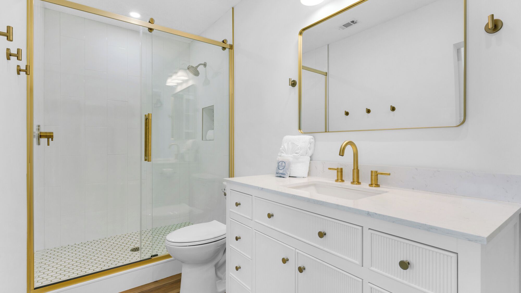 A modern bathroom with a glass-enclosed shower, a white toilet, and a vanity with a sink and mirror.