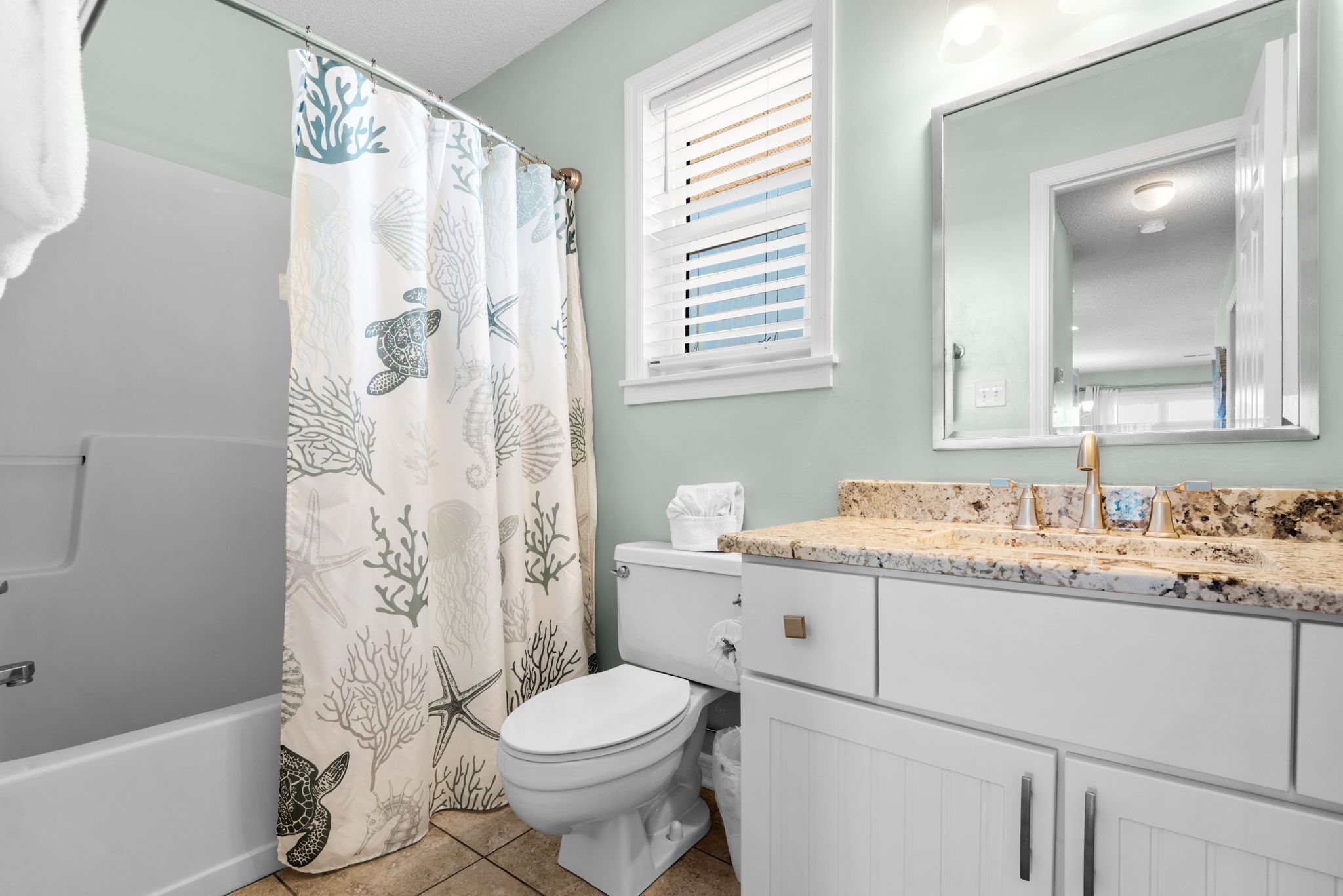 A bathroom with a shower curtain featuring sea life, a toilet, a sink with a granite countertop, and a mirror above the sink.