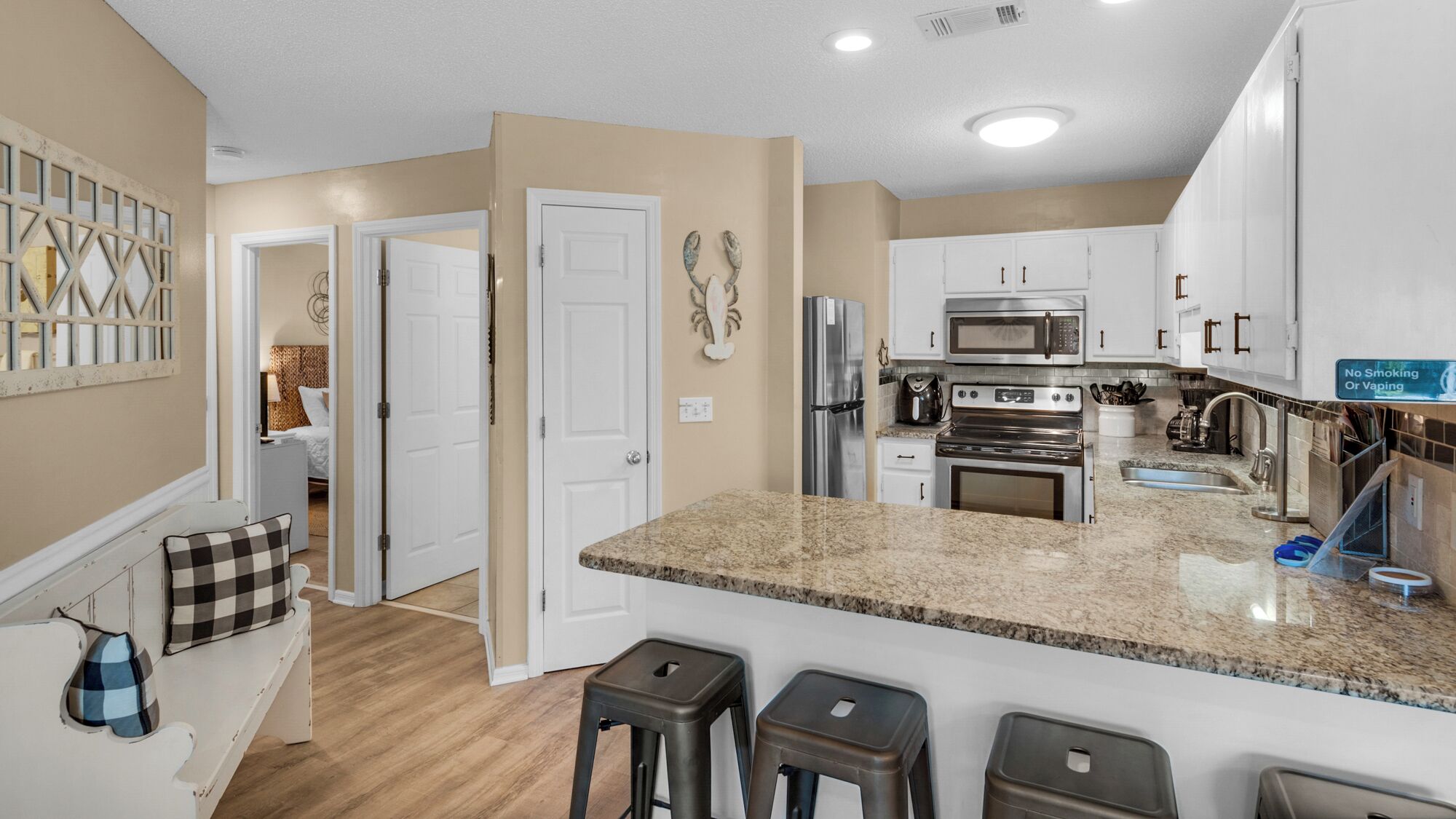 A modern kitchen with granite countertops, stainless steel appliances, and a 'No Smoking Or Vaping' sign.