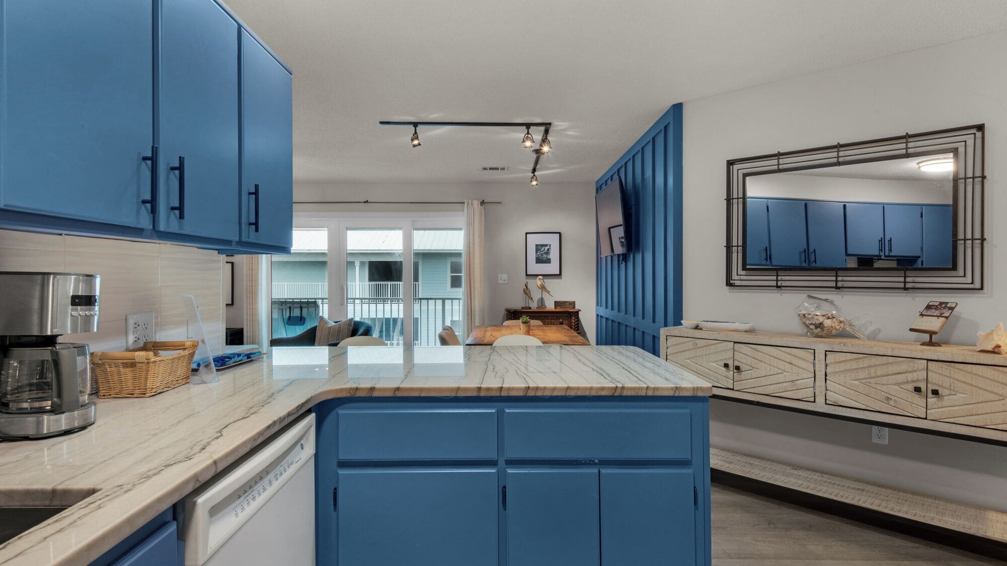 A modern kitchen with blue cabinets, a marble countertop, and a large mirror.