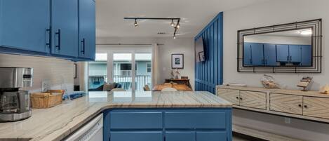 A modern kitchen with blue cabinets, a marble countertop, and a large mirror.