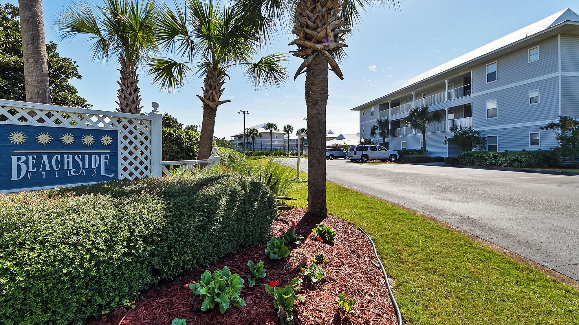 A sign for Beachside Village with a well-maintained lawn and palm trees.