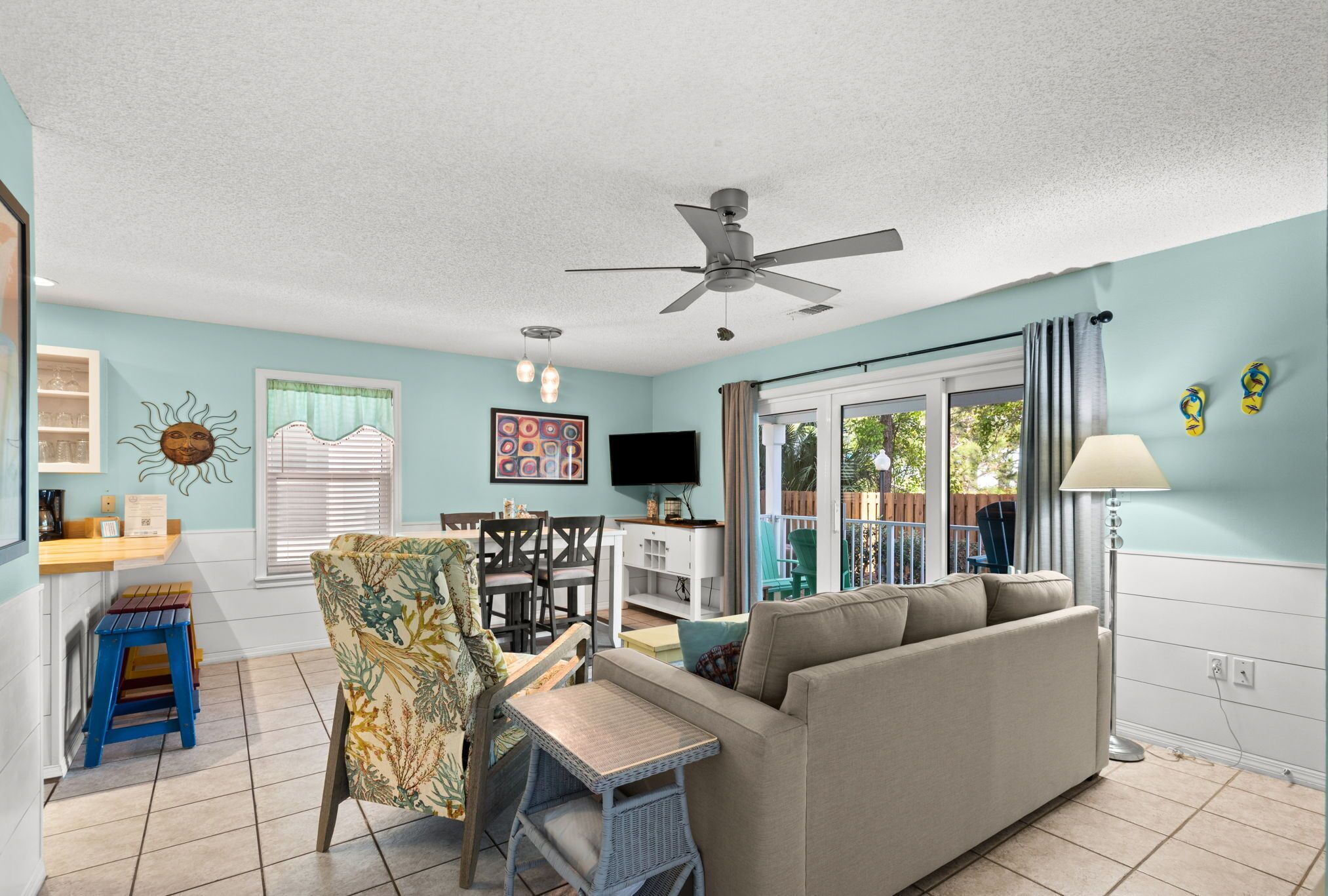 A living room with a sofa, a dining table, chairs, a ceiling fan, a TV, and a window with curtains.