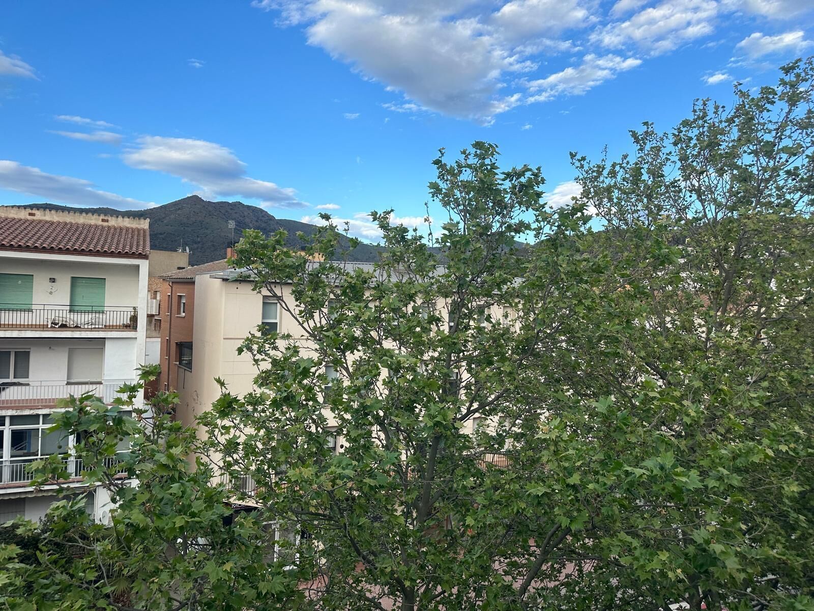 A residential building with a balcony, a mountain in the background, and a clear sky.