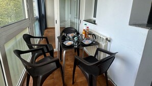 En lille balkon med et bord dækket til to personer, stole, en radiator og et vindue med gardiner.