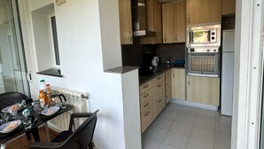 Et kompakt køkken med træskabe, indbygget ovn, mikroovn og et spiseområde med bord og stole.