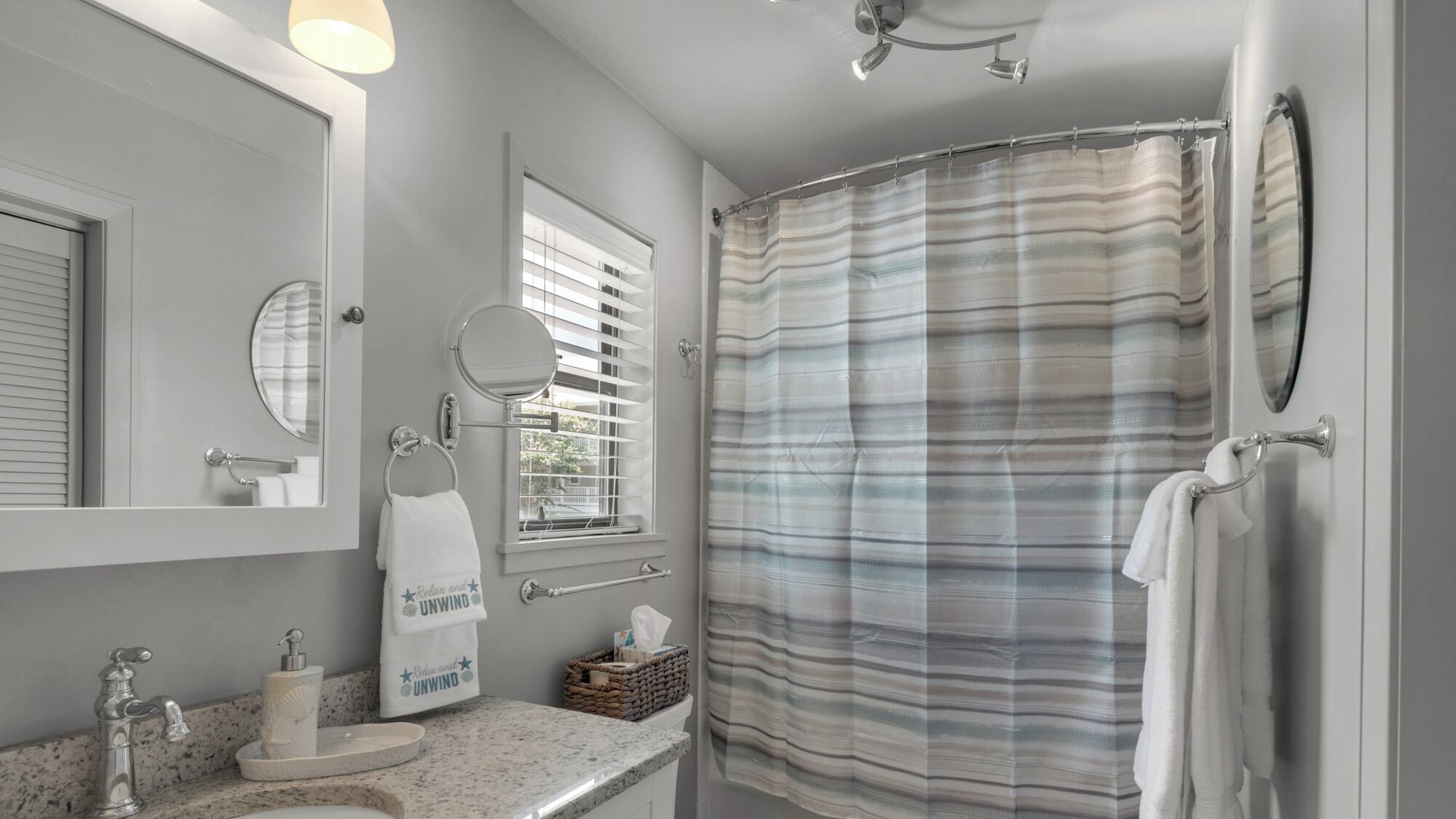 A bathroom with a shower curtain, a sink with a towel, a mirror, and a window with blinds.