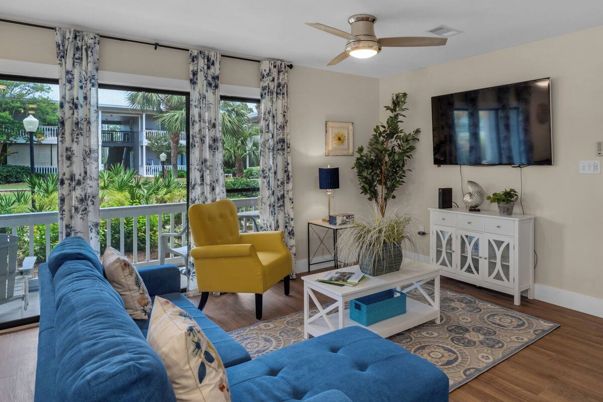 Una sala de estar con un sofá azul, un sillón amarillo y un mueble blanco con un televisor encima.