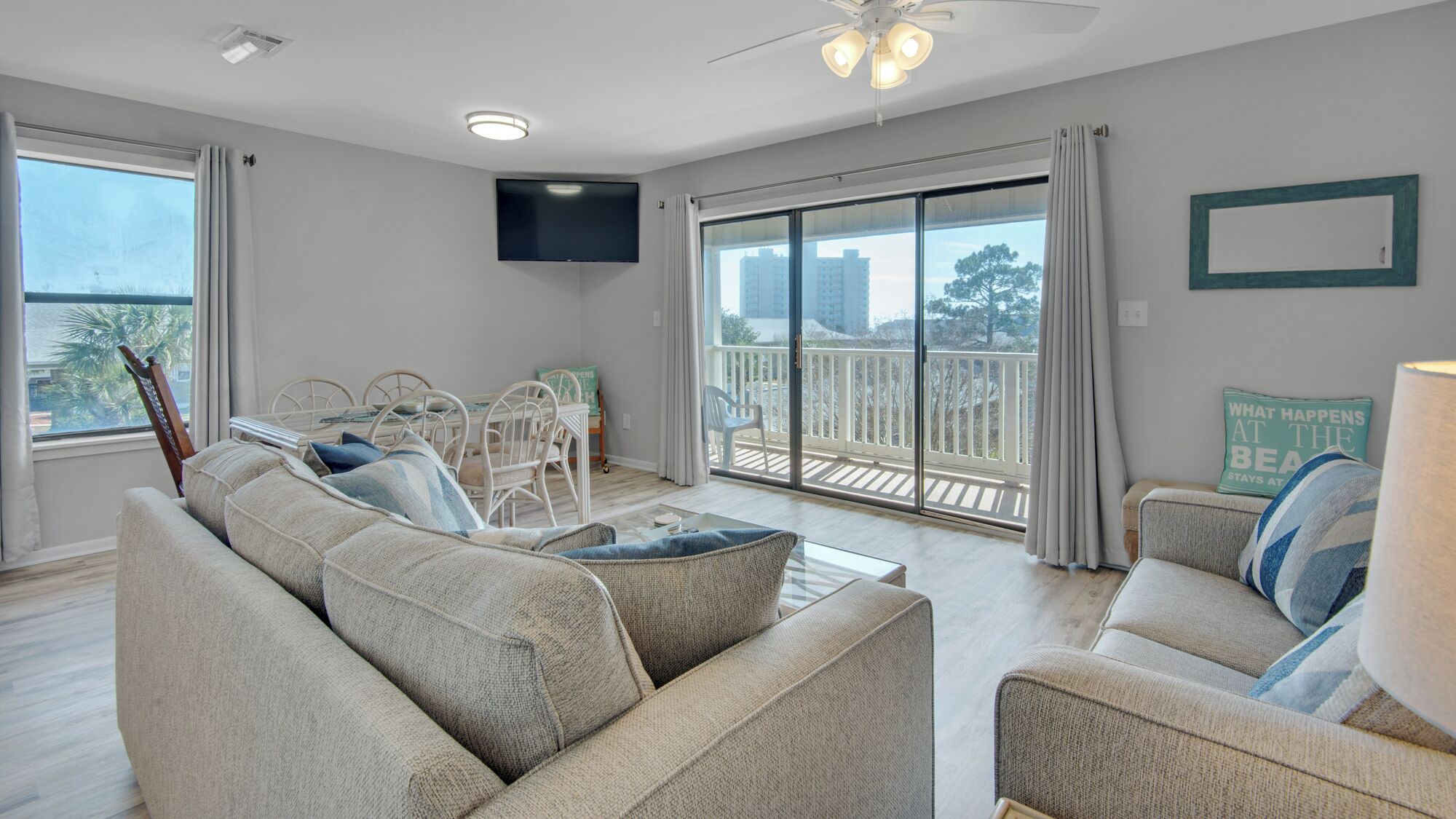 Een ruime woonkamer met een grote bank, een eettafel met stoelen, een flatscreen-televisie aan de muur en een balkon met uitzicht over de stad.