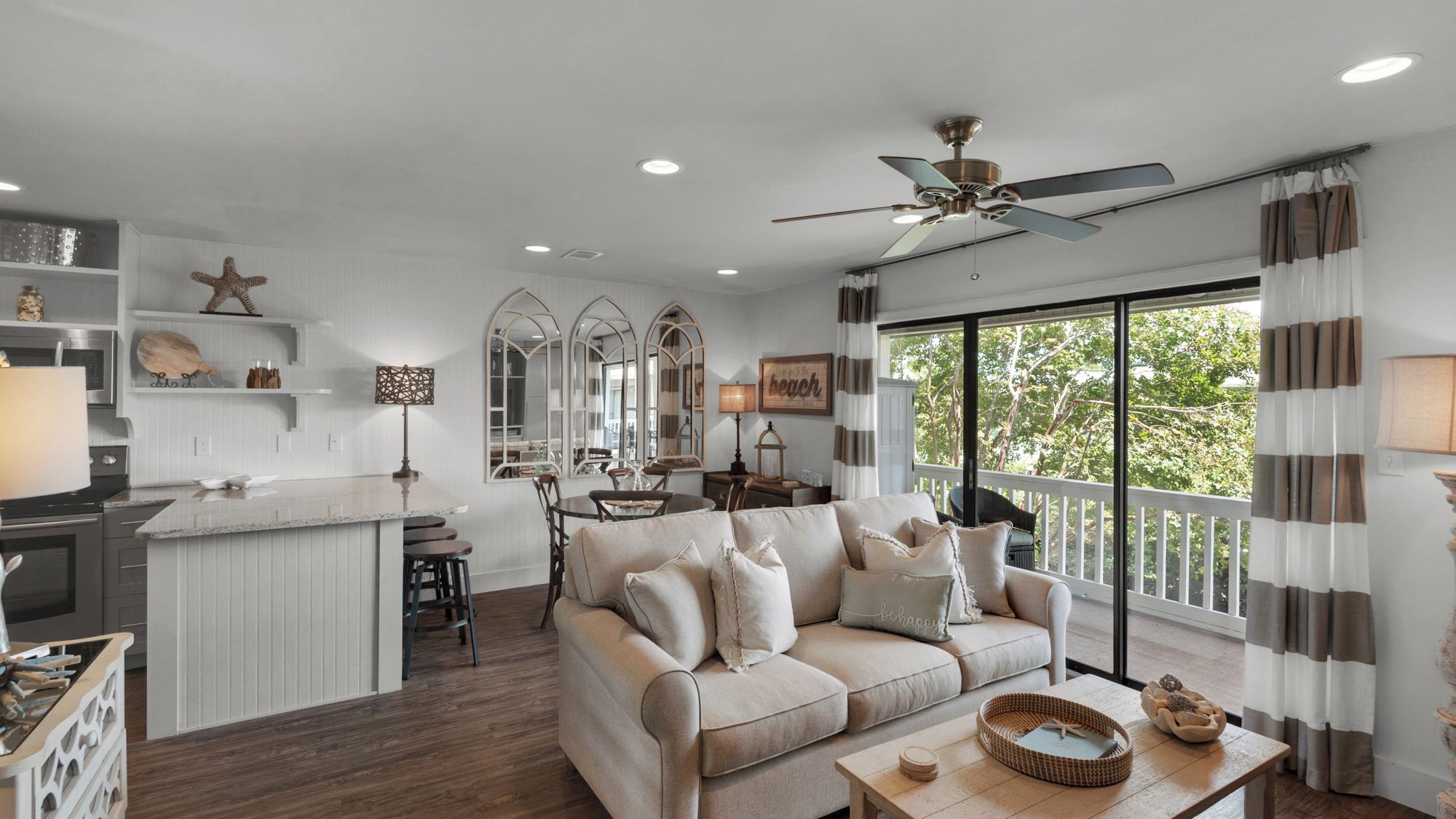A spacious living area with a large window, a ceiling fan, and a kitchen with white cabinetry.