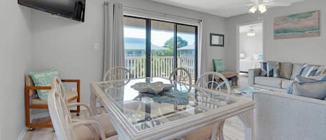 A spacious living room with a glass dining table, white wicker chairs, a grey sofa, and a ceiling fan.
