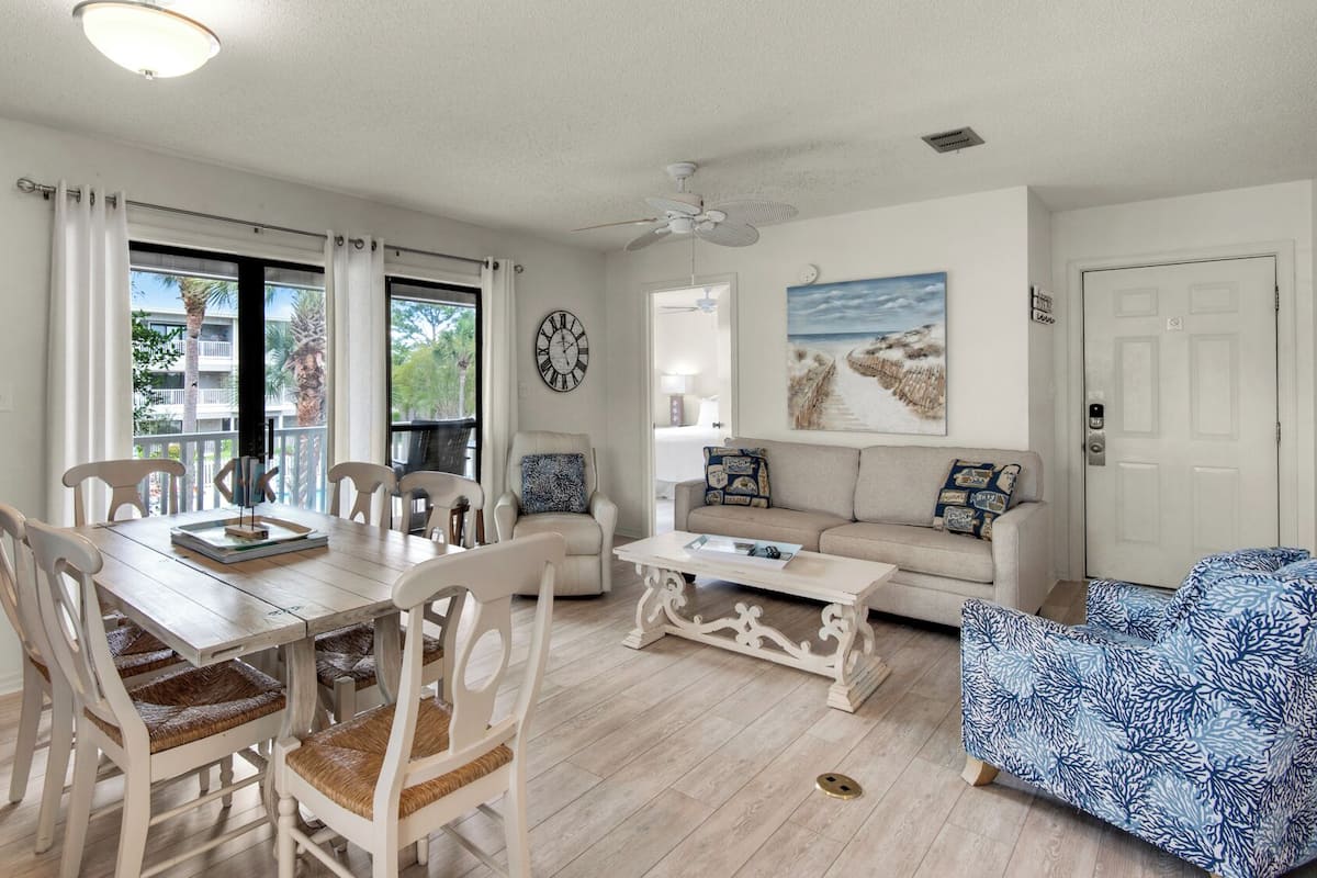 A living room with a dining area, a sofa, a coffee table, and a chair with a patterned cushion.
