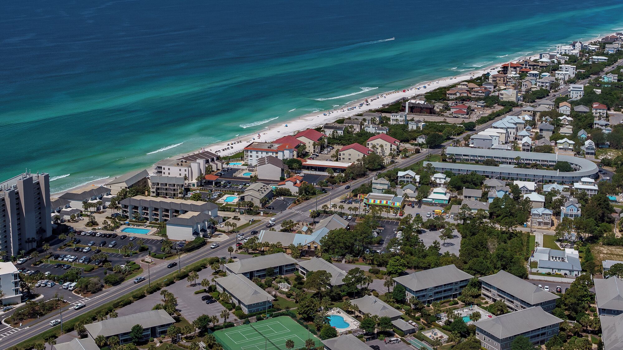 An aerial view of a coastal town with a beach, residential buildings, and a large hotel complex.