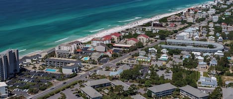 An aerial view of a coastal town with a beach, residential buildings, and a large hotel complex.