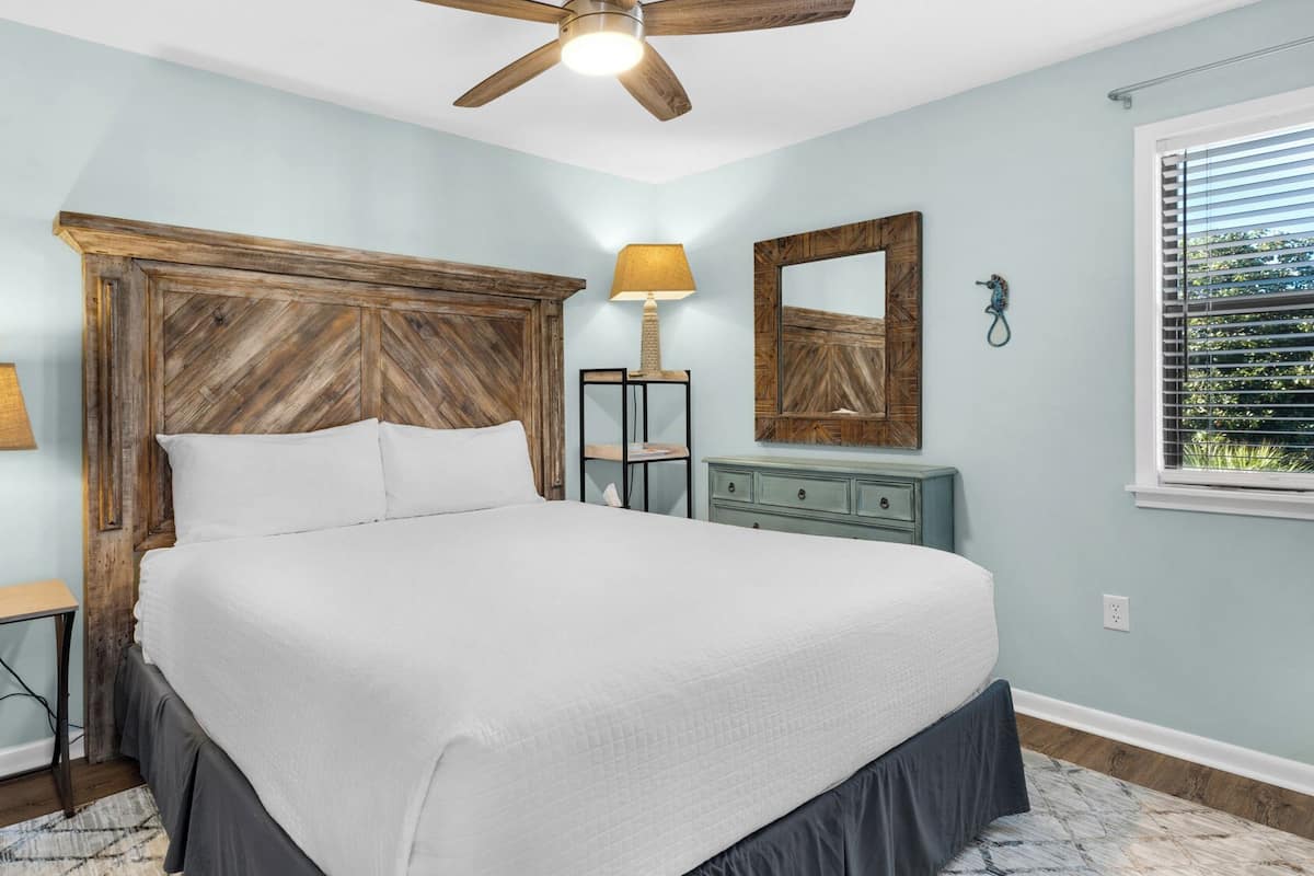 A bedroom with a bed, a nightstand, a dresser, a ceiling fan, a mirror, and a window with blinds.